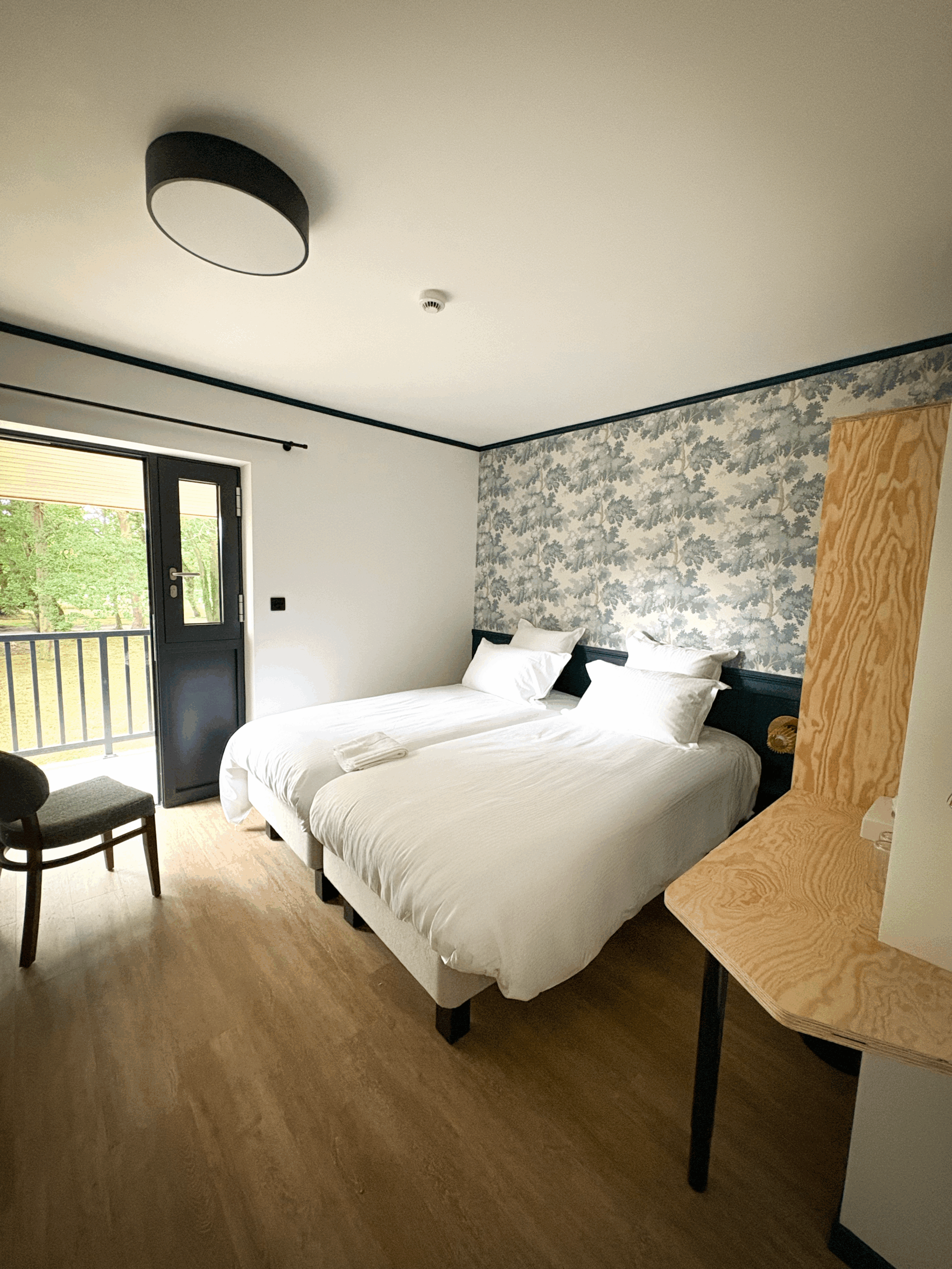 Image avec lumière naturelle de la pièce principale d'une chambre twin bleue de l'hôtel du golf de Jumièges, on y voit un petit bureau avec la corbeille de bienvenue de l'hôtel